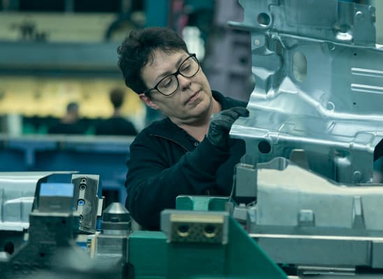 Ein Mitarbeiter mit Brille steht an einer Maschine und bearbeitet Metall.