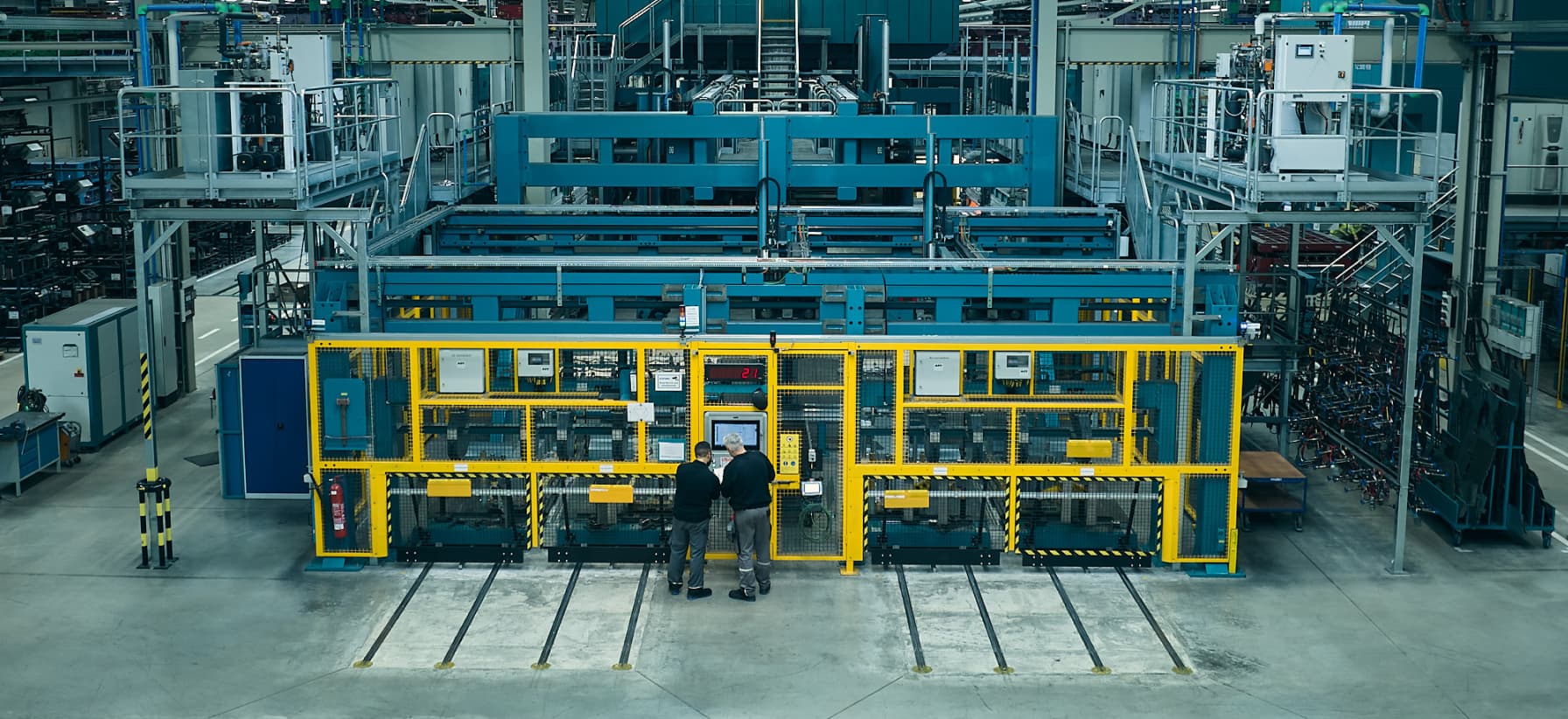 Eine Große Werkshalle des Unternehmens GEDIA. Zwei Männer stehen an einer Maschine und arbeiten.